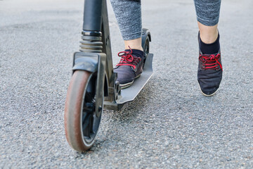 View of the legs of a woman riding a scooter on asphalt.