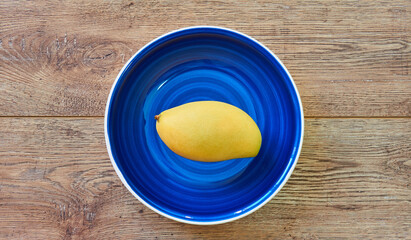 pale yellow mango on a blue plate on a wooden tabletop
