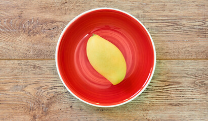 pale yellow mango on a red plate on a wooden tabletop