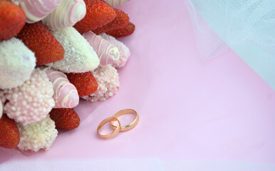 Gold wedding rings and a bouquet of strawberries in chocolate on a pink background, copy space