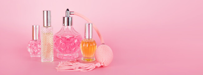 Different transparent perfume bottles on pink background. Aromatic essence bottles. Perfumery,...