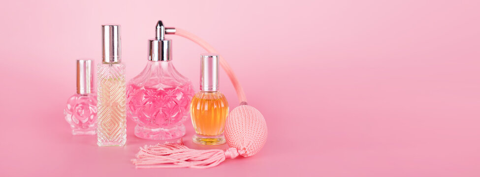 Different transparent perfume bottles on pink background. Aromatic essence bottles. Perfumery, cosmetics, fragrance collection. Banner, free space for text.