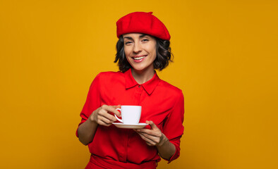 A delicious break during a journey! Half-lenght photo of a young tourist, dressed in parisian style, with a red beret, spends her journey time with a cup of delicious coffee.