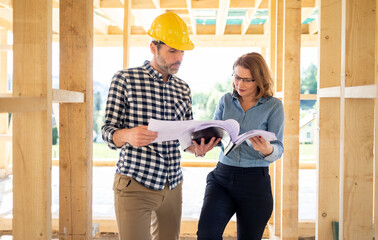 Female homeowner consults blueprints with architect or engineer on construction site of her new...