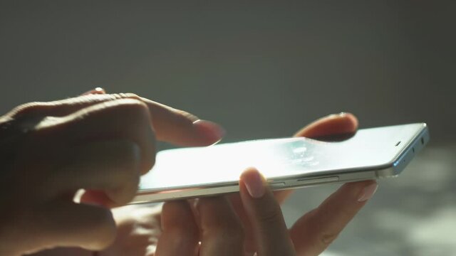 close up woman hand holding wite telephone smart phone screen golden sun light sunshine background sunny day internet searching application store notification weblink online video call