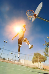 Man about to slam dunk ball on basketball court with strong sun shining lensflare