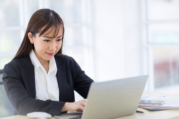 Beautiful Asian businesswomen  wearing a black suit is smiling confidently while typing labtop. Asian business women Concept