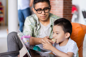 Father feeds a child while watches a tablet at home