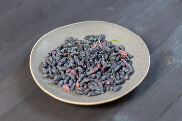 Gray plate with ripe blue honeysuckle berries on black wooden background