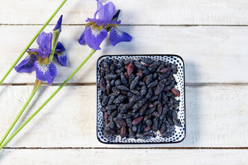 Plate with ripe blue honeysuckle berries and iris flowers on white wooden background