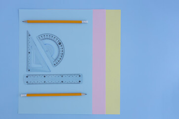 colored paper, triangle, ruler, protractor, pencils on a blue background. back to school concept