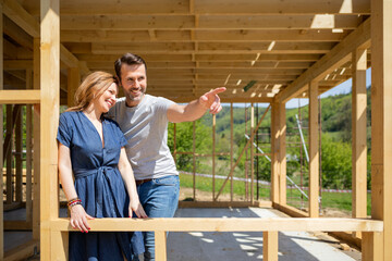 Couple standing on future window in construction site of their new house, dreams come true