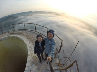 Camping on top of a smoke stack chimney, surrounded by fog and mist underneath the top of the building, sunrise