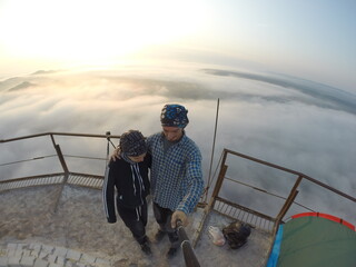 Camping on top of a smoke stack chimney, surrounded by fog and mist underneath the top of the building, sunrise