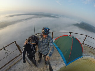Camping on top of a smoke stack chimney, surrounded by fog and mist underneath the top of the building, sunrise