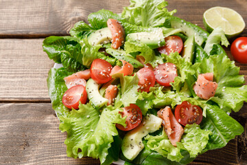 Salmon salad with avocado, green leaves and tomatoes on wooden table