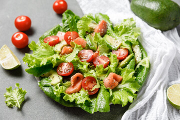 Salmon salad with avocado, green leaves, tomatoes on gray background