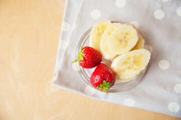 strawberry and banana on a glass plate on a wooden background.