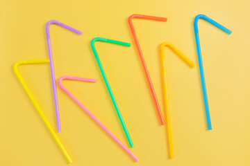 Multi-colored plastic tubules on a yellow background. The concept of a birthday party. Red, orange, yellow, blue, green, swarm, purple.