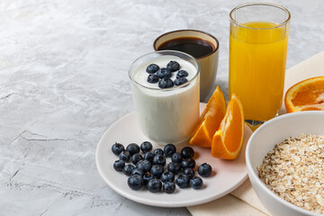 Fototapeta na wymiar breakfast with yogurt with blueberry and juice, orange, oatmeal and coffee on concrete background