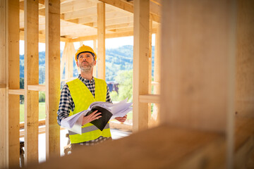 Construction engineer or architect with blueprints visiting building site of wood frame house
