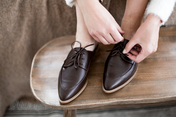 fashionable women's shoes, feet in the interior, classic women’s flat shoes, brown leather shoes, mules and loafers, knitted blankets and blankets on the background, wooden background, cotton flowers,