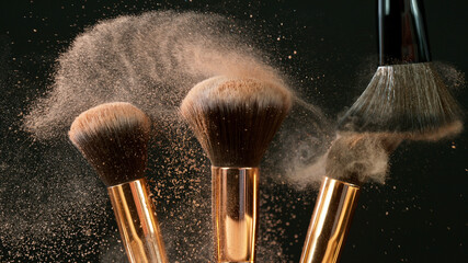 Makeup brushes touch each other on dark background and small particles of cosmetics