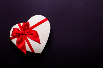 White gift in the shape of a heart with a red bow on a dark background close-up. Place to insert text
