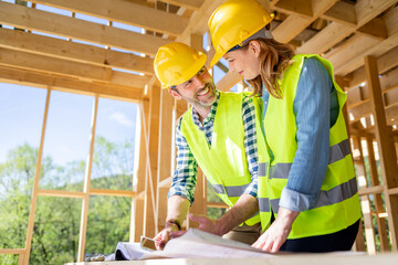 Construction engineer and architect consult plans on building site of wood framing house under construction