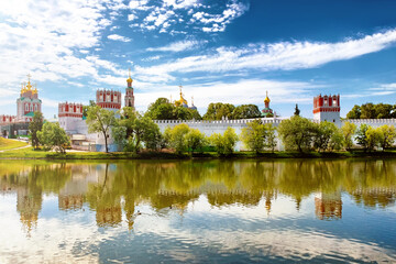 Fototapeta na wymiar famous moscow city novodevichy convent landmark with golden domes and scenery reflection on park pond water against scenic blue sky with clouds background. Wide view