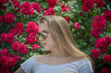portrait of a young beautiful girl in glasses on a background of flowers of red roses