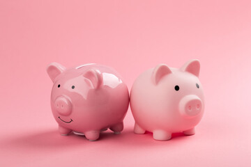 Two pink piggy banks on a pink background.