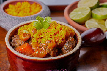 Beef curry in a bowl,with some rice and lime segments in the background.