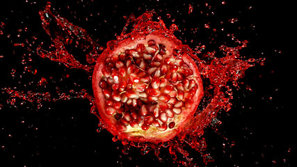 Freeze motion of sliced pomegranate with splashing juice isolated on black background
