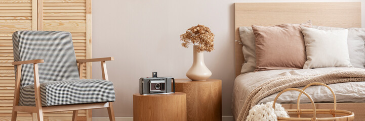 Retro armchair, wooden bedside tables and bed in a cozy bedroom interior