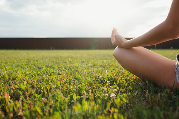 Close-up of the leg and hands of a girl sitting in a lotus position on a green lawn, far horizon and blue sky