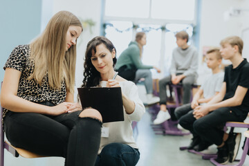 Elegant young teacher checks the attendance list during additional workshops at school