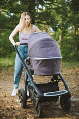 Beautiful blonde woman with her baby in baby carriage in forest