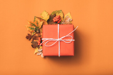 Holiday present. Greeting. Gift box. Fall leaves decorative composition. Orange background.