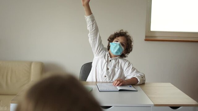 Children in the class after quarantine coronavirus covid-19, back to school, post-quarantine life. Curly masked schoolboy pulls his hand up, ready to answer