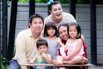 Large family living together. There are parents, aunts and brothers and sisters together to take pictures happily in house. Some children wear medical masks on wrists. Boy suck fingers. Warm family.