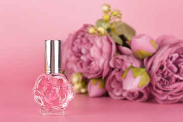 Obraz na płótnie Canvas Transparent perfume bottle with bouquet of peonies on pink background. Aromatic essence bottle with spring flowers. Perfumery, cosmetics, fragrance collection.