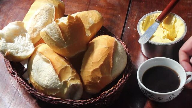 Hand picking up coffee cup, in a table with basket of "French bread", traditional Brazilian bread