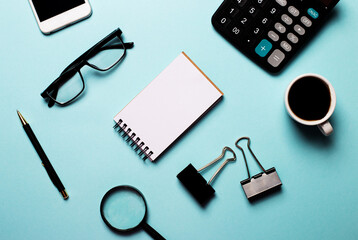 A pen, a telephone, glasses, a flower in a pot and a cup of coffee lie on a blue background. Business concept