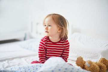 Happy toddler girl in striped red and white pajamas sitting on bed