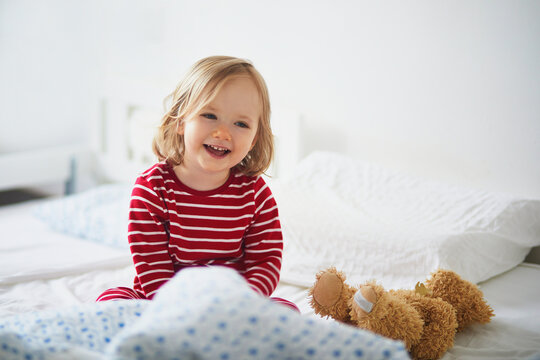 Happy toddler girl in striped red and white pajamas sitting on bed