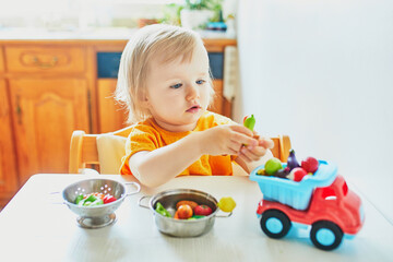 Adorable little girl playing with toy fruits and vegetables at home