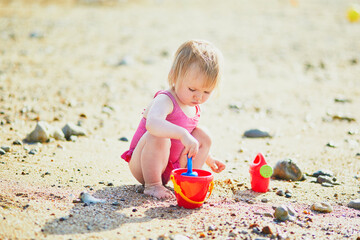 Adorable toddler girl playing with sand on the beach. Child spending vacation on the Atlantic coast in Normandy, France. Outdoor activities for kids