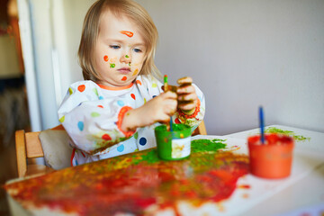 Adorable little girl painting with brushes and fingers