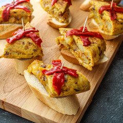 Spanish tortilla pintxo on a wooden board. Potato omelette on bread as a basque canape on sharing board. Party food. 